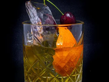 Glas mit Eis, einer Kirsche und Orangenscheibe, dunkel.