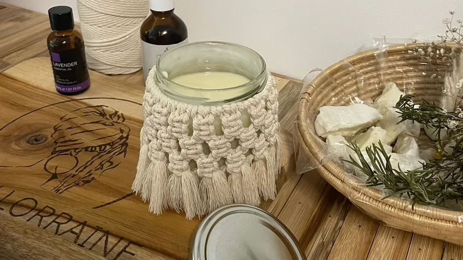 Candle in macramé holder on wooden table.