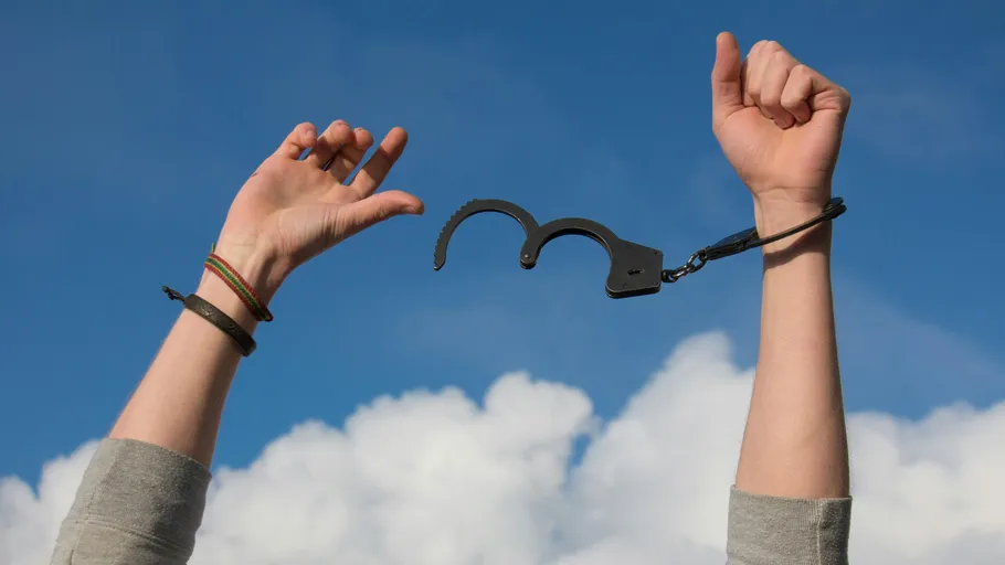 Hände befreien sich von offenen Handschellen gegen Himmel.