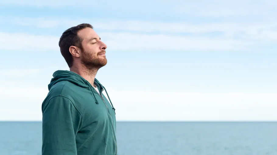 Mann im grünen Hoodie atmet am Meer.