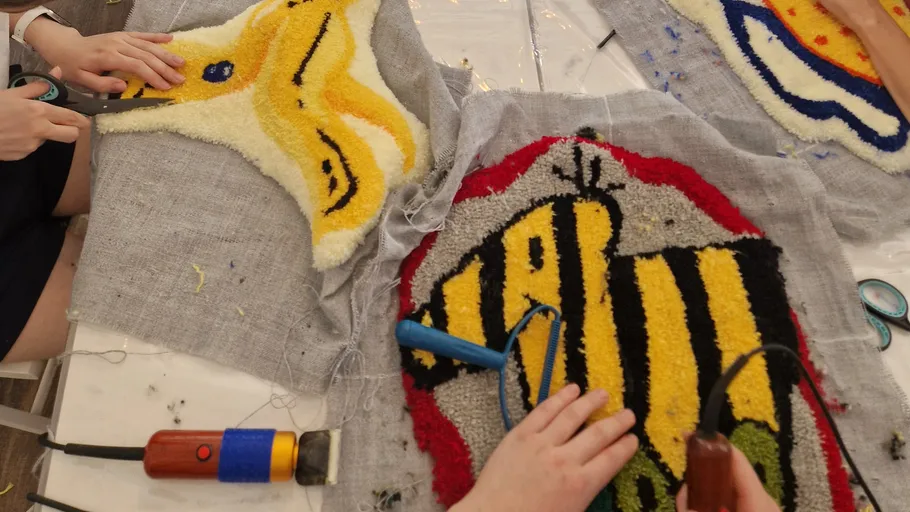 Hands crafting colorful tufted fabric designs.