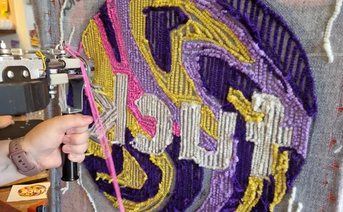 Hand using tufting gun on colorful rug.