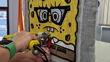 Person tufting cartoon character into textile frame.