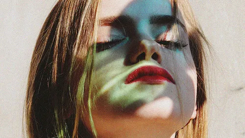 Woman's face with colored shadows outdoors.
