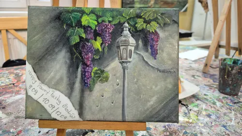 Painting of grapes and a lamp on easel.