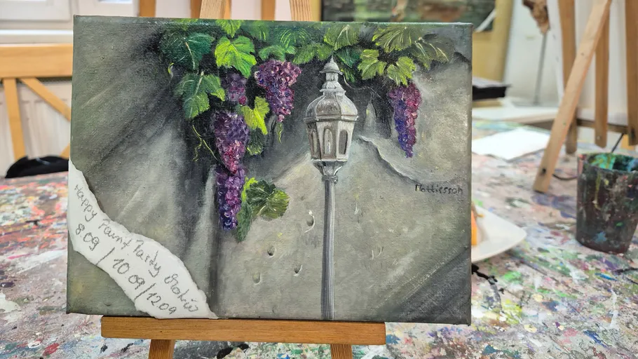 Painting of grapes and a lamp on easel.
