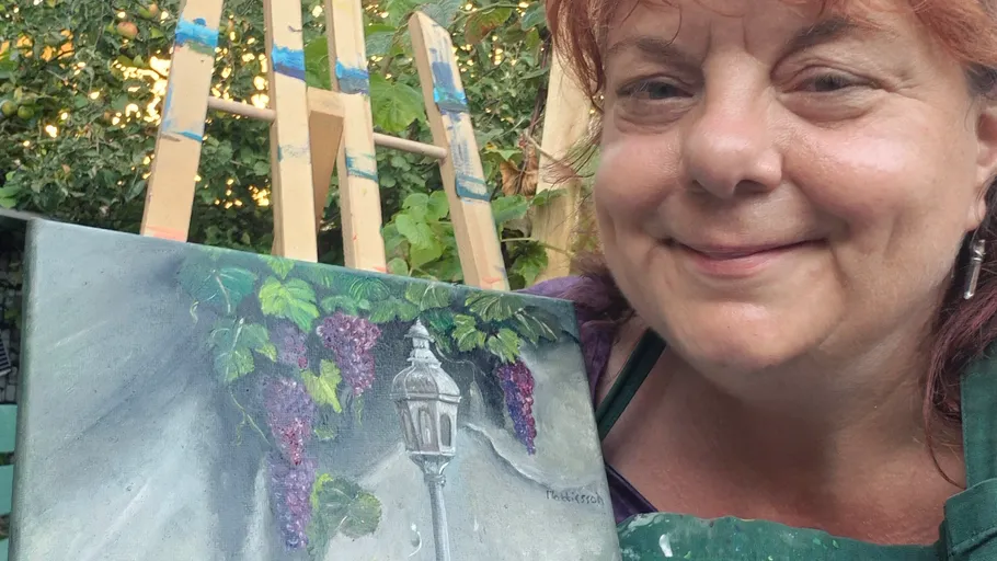 Artist smiling next to their painting outdoors.