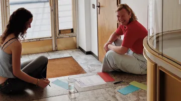 Zwei Personen sitzen mit Papieren auf dem Boden.
