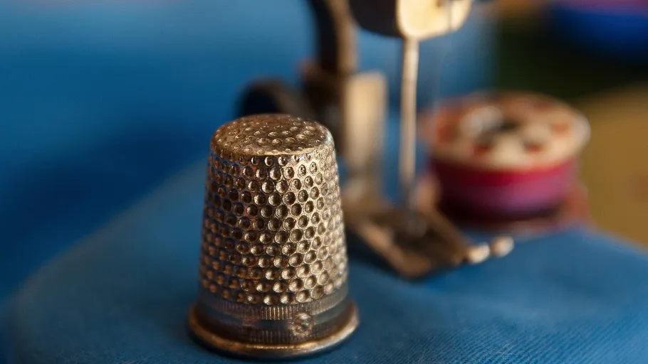 Thimble on blue fabric, sewing machine nearby.