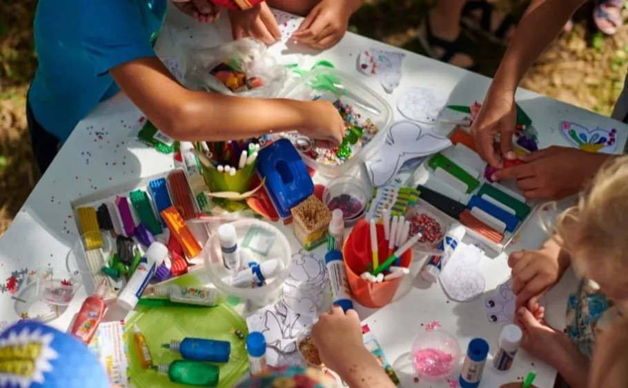 Kinder basteln an einem Tisch mit Kunstbedarf im Freien.