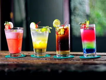 Vier bunte Cocktails stehen auf einem Holztisch.