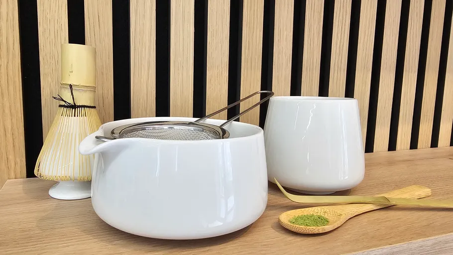 Matcha-Besen, Kanne, Tasse und Löffel auf Regal.