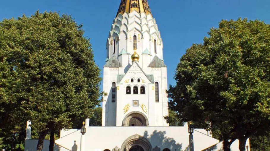 Weiße Kirche mit Turm, umgeben von Bäumen.