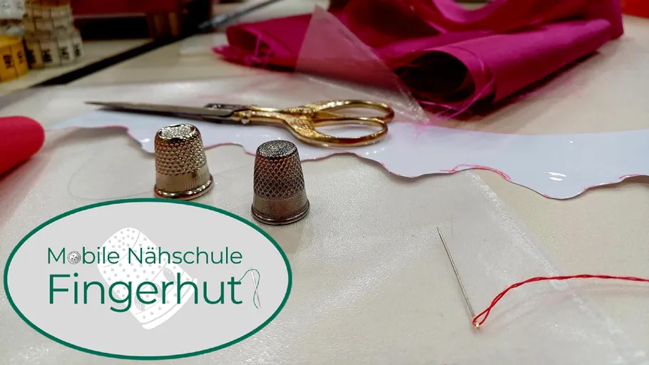 Schere, Fingerhüte, Nadel, roter Stoff auf Tisch.