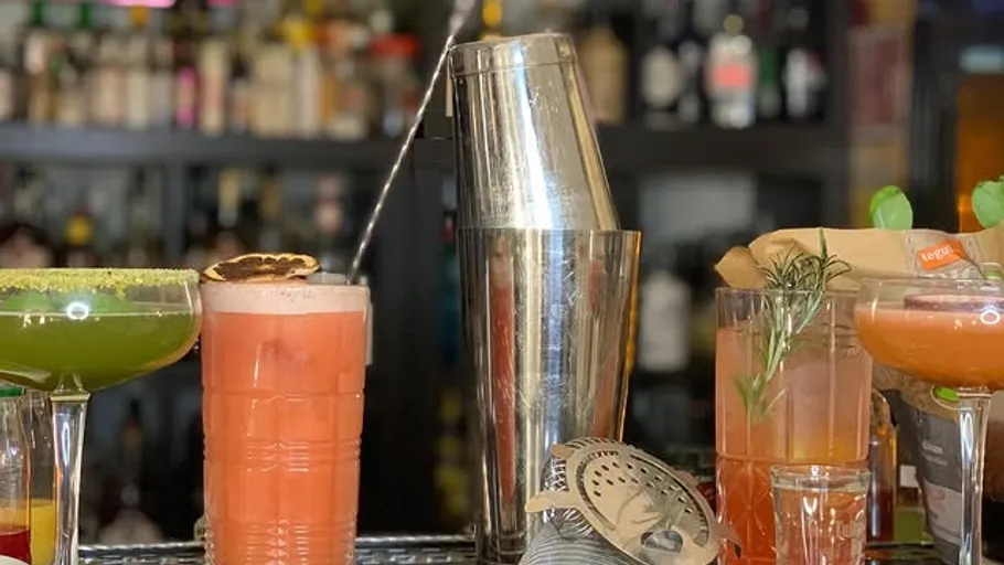 Colorful cocktails with shaker on bar counter.