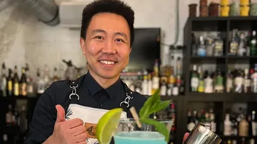 Smiling bartender gives thumbs up in bar.