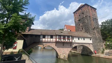 Historische Brücke mit Haus und Turm über Fluss.