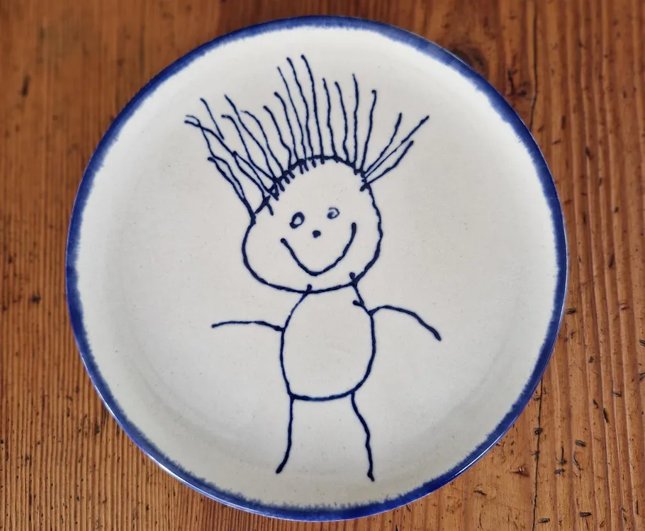Teller mit Kinderzeichnung, Holztisch.
