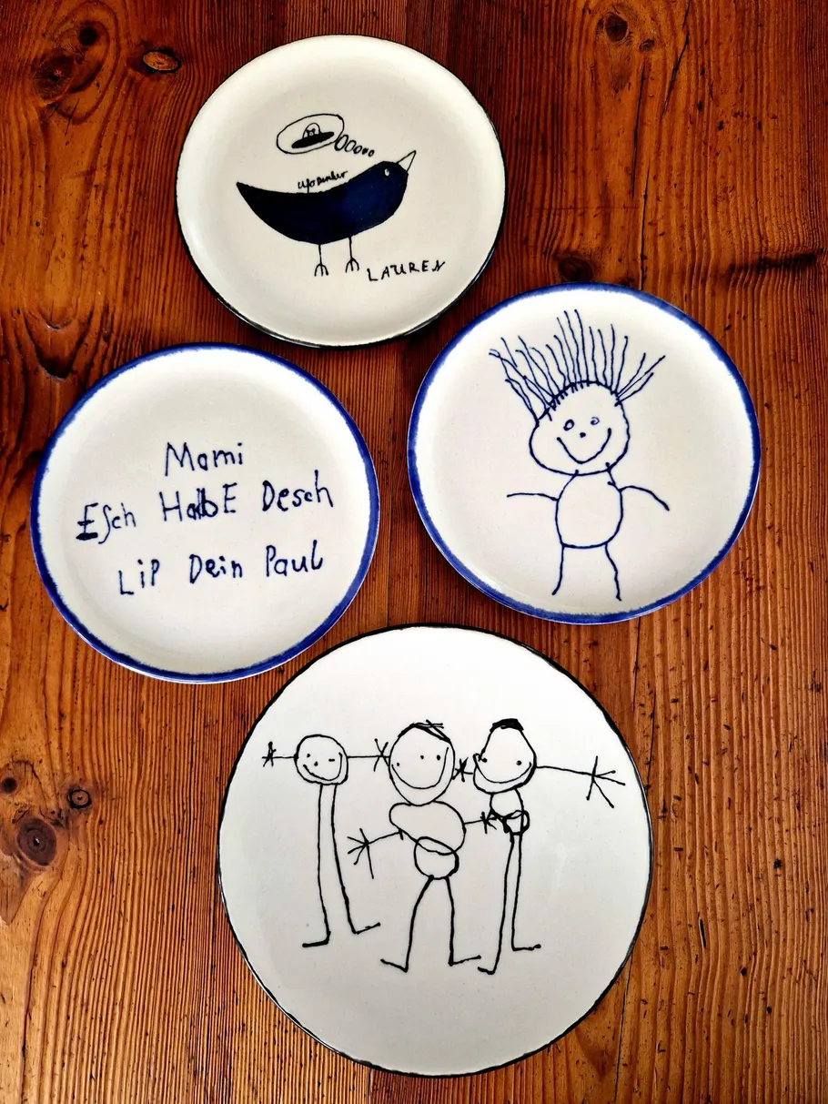 Teller mit Kinderzeichnungen auf Holztisch.