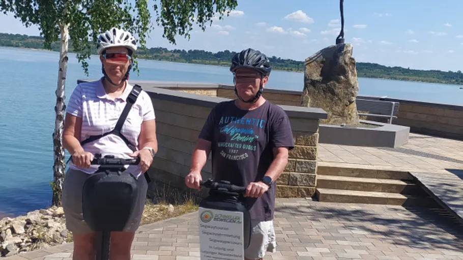 Two people riding segways near a lake.