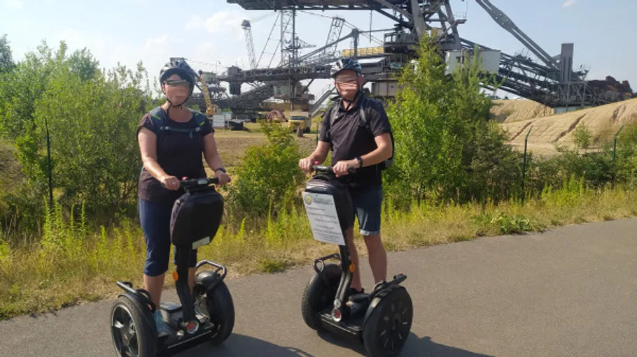 Two people riding Segways near industrial site.
