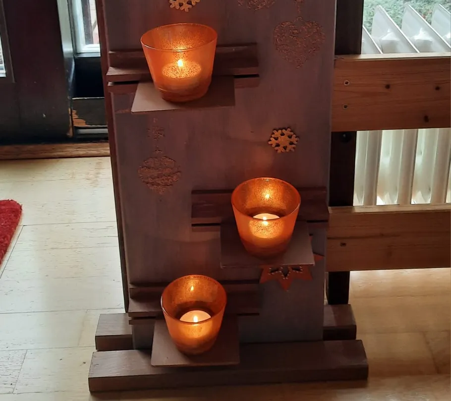 Three lit candles on a wooden shelf indoors.