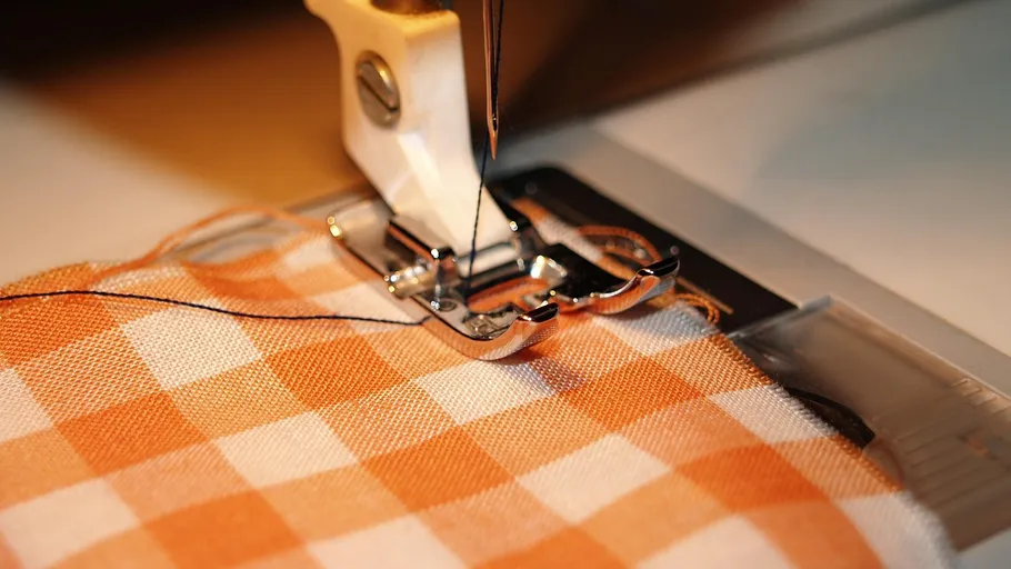 Nähmaschine näht orange karierten Stoff.