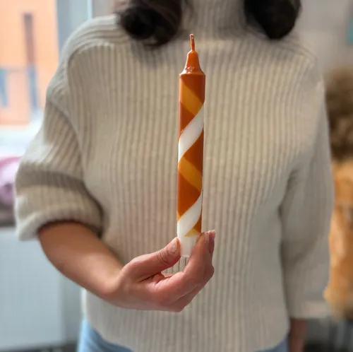 Person holds twisted orange-white candle indoors.