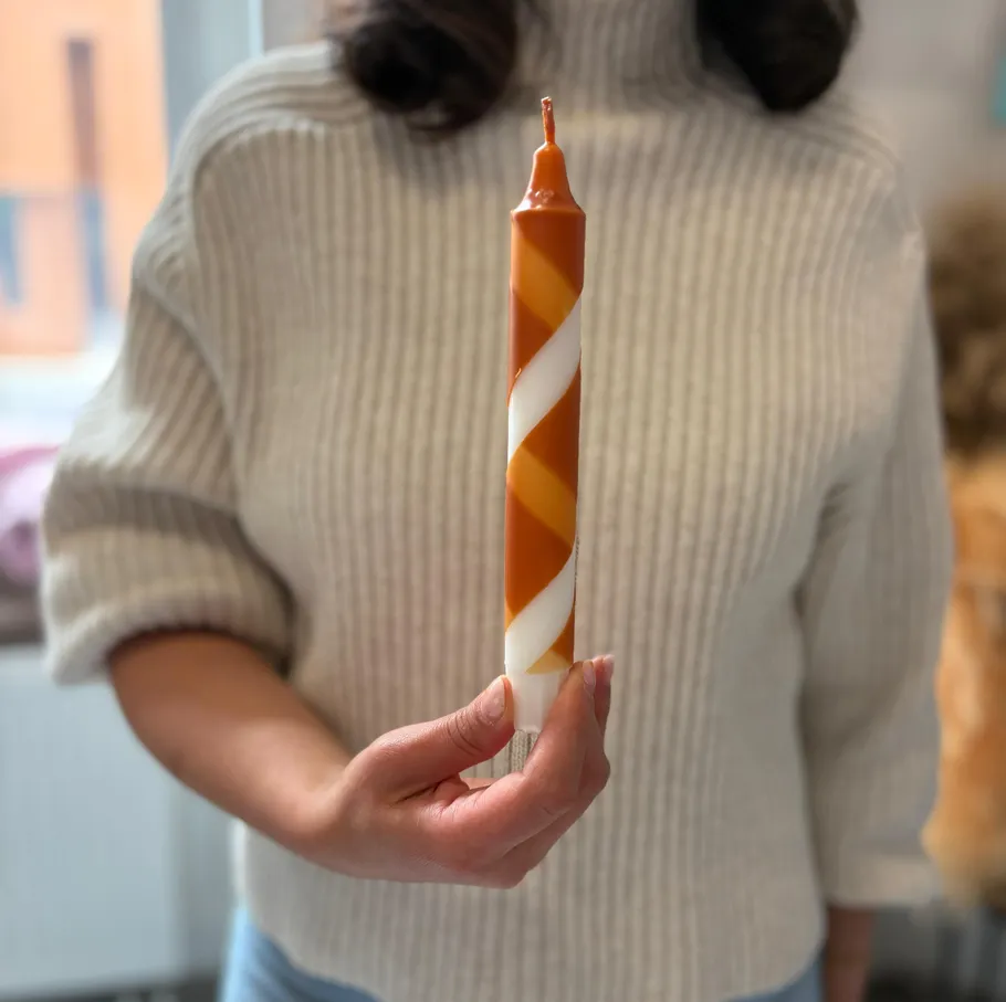 Person hält verdrehte orange-weiße Kerze drinnen.