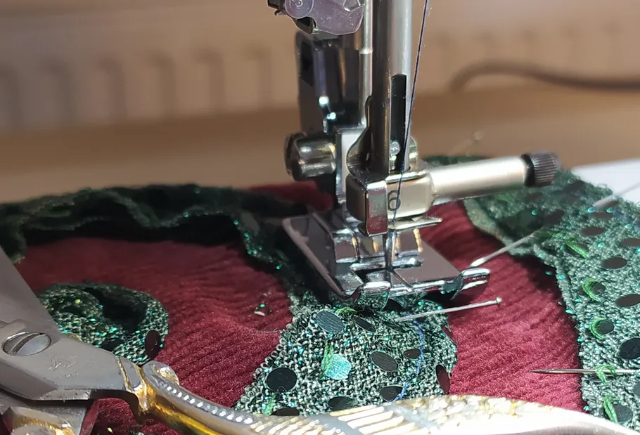 Nähmaschine näht grünen Stoff auf rotem Stoff.