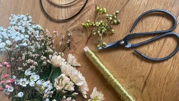 Flowers, wire, and scissors on wooden table.