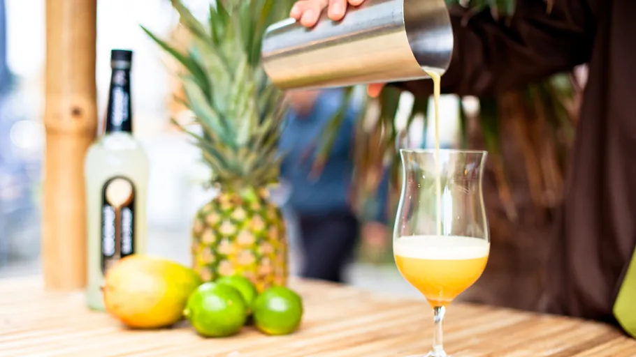 Person pouring cocktail near fruits and bottle.
