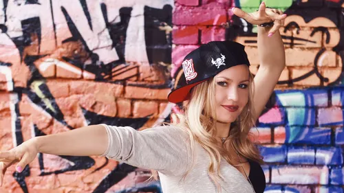 Woman dancing energetically by graffiti wall.