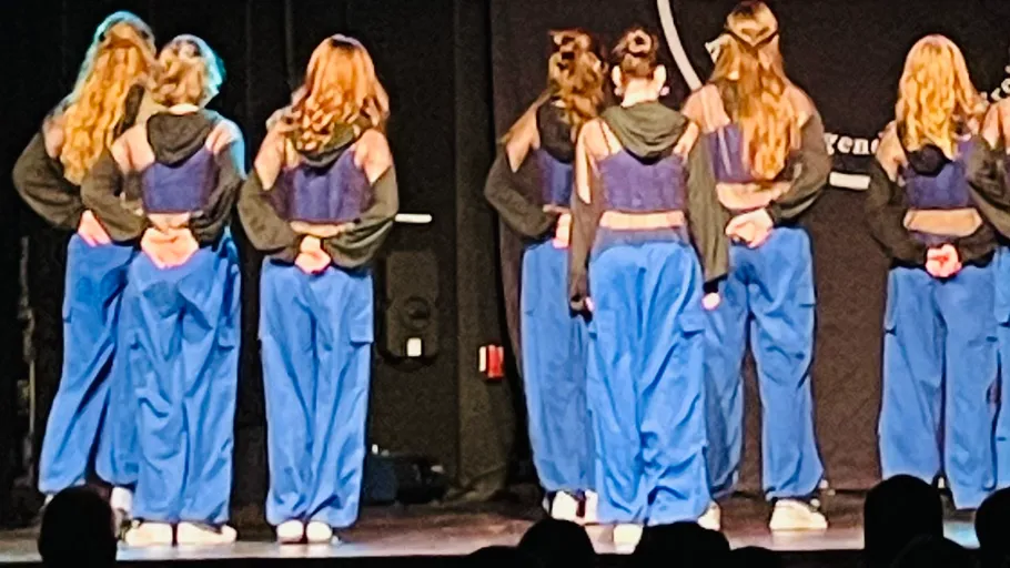 Dancers standing on stage in blue outfits.