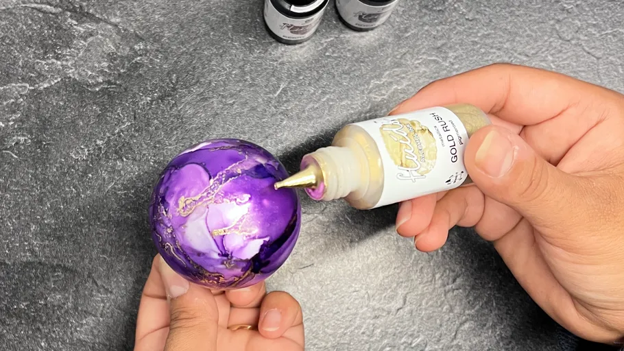 Hände verzieren lila Kugel mit Goldfarbe.