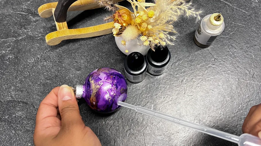 Hand painting ornament with pipette, bottles nearby.