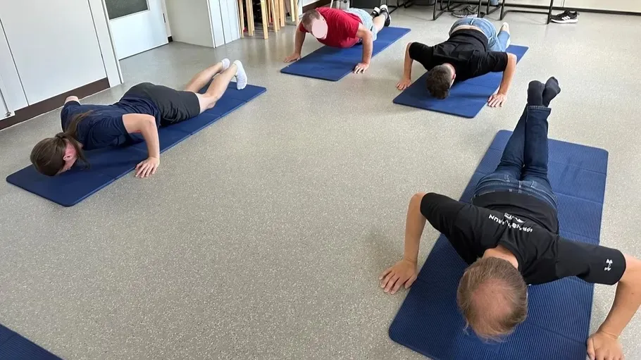 Four people doing push-ups on mats indoors.