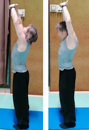 Person stretching arms upward on yoga mat indoors.
