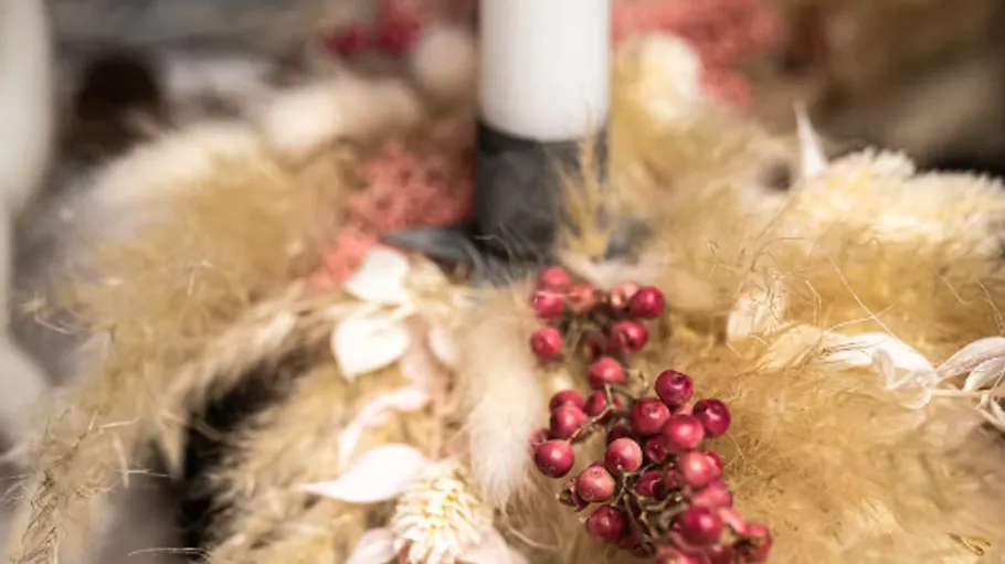 Candle surrounded by dried flowers and berries.