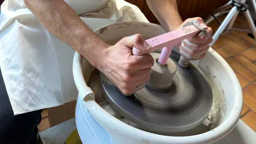 Person using pottery wheel tool indoors.