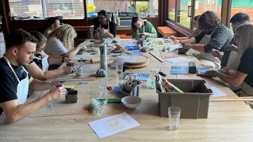 People sculpting clay at a workshop table.