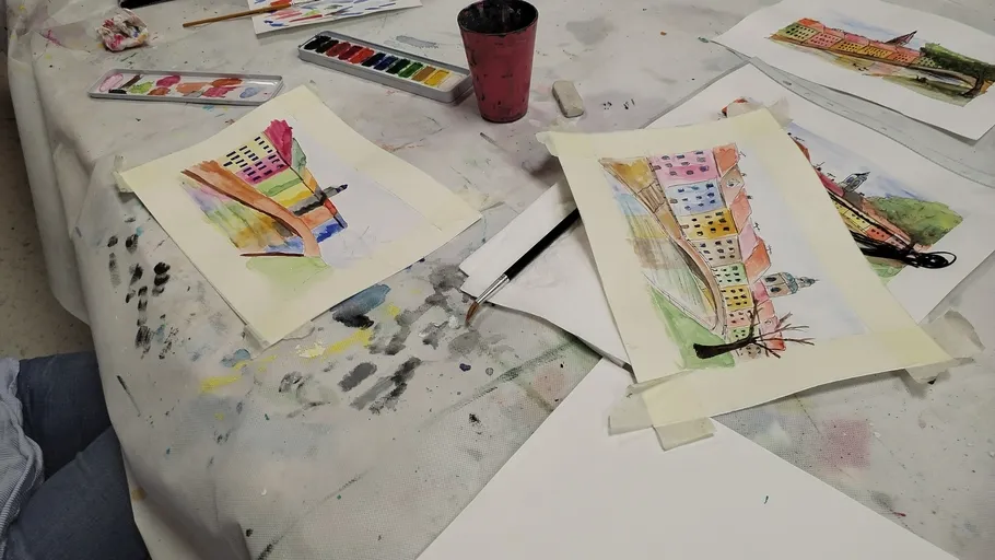 Two paintings of colorful buildings on messy table.