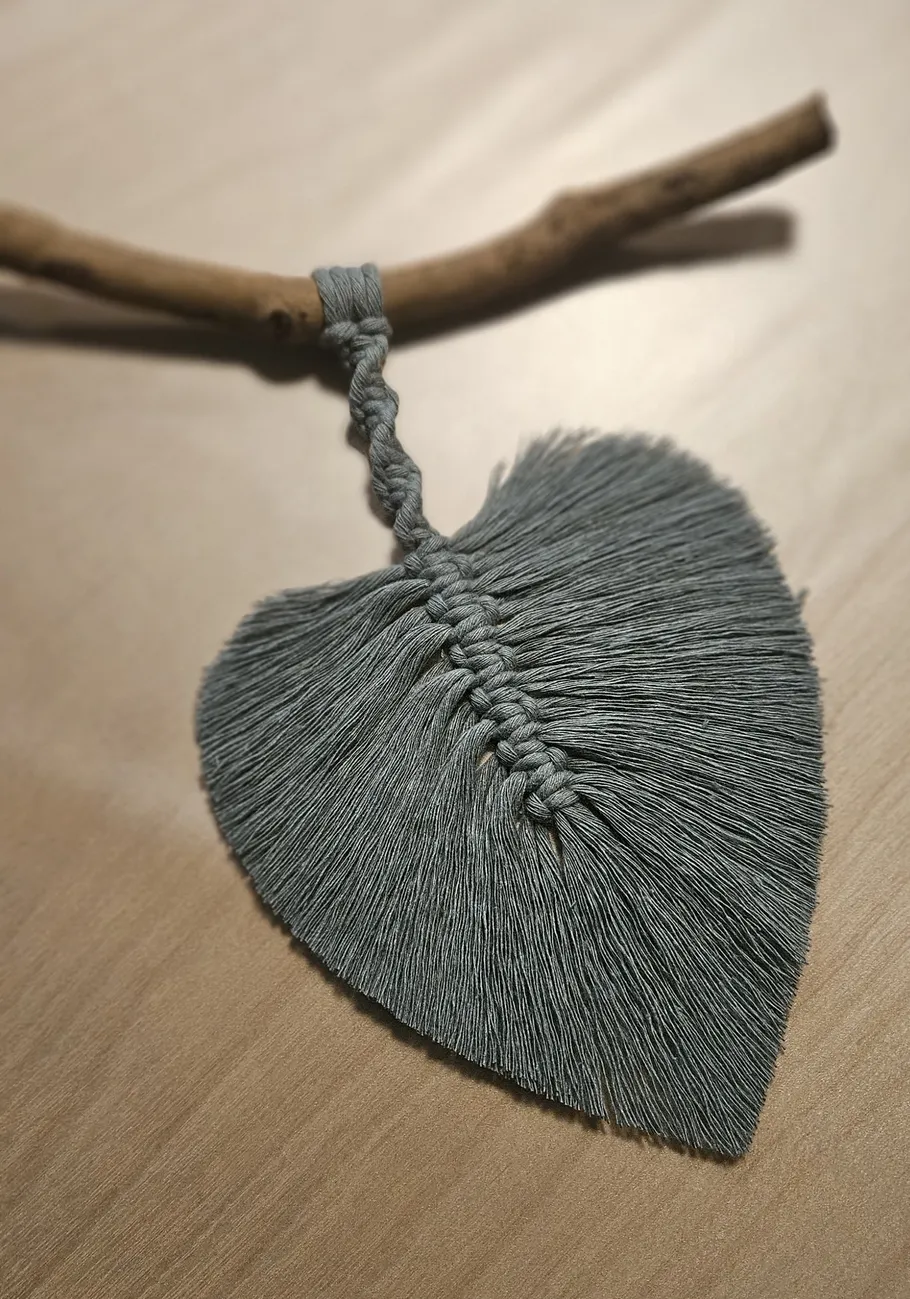 Herzförmiges Makramee hängt an Holzstab.
