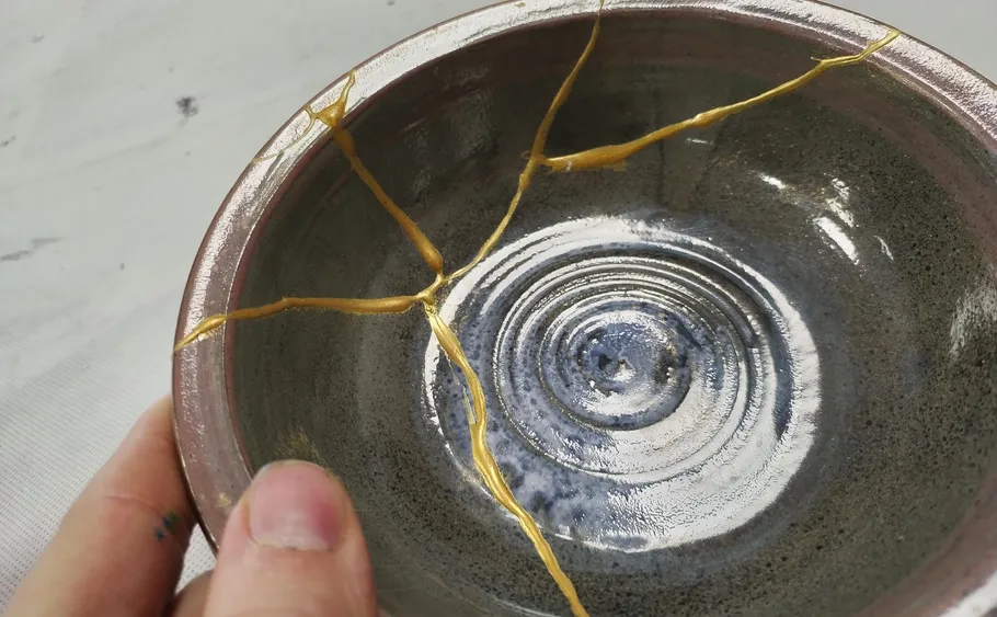 Hand hält Keramikschale mit Gold repariert.