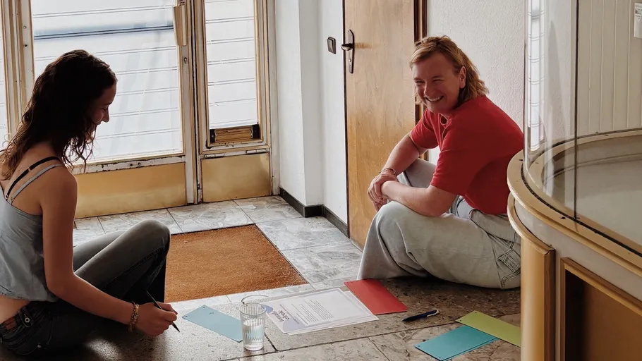 Two people sit on floor with paperwork.