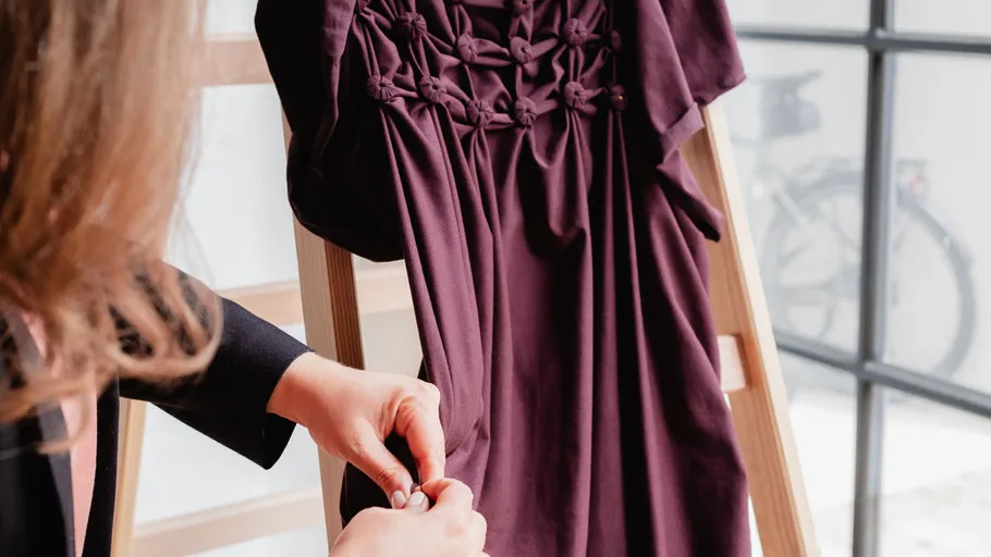 Person passt plissiertes bordeauxrotes Kleid auf Leiter an.