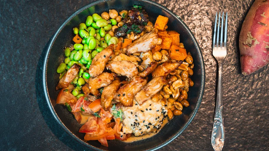 Schüssel mit Hühnchen, Gemüse auf dunkler Oberfläche.