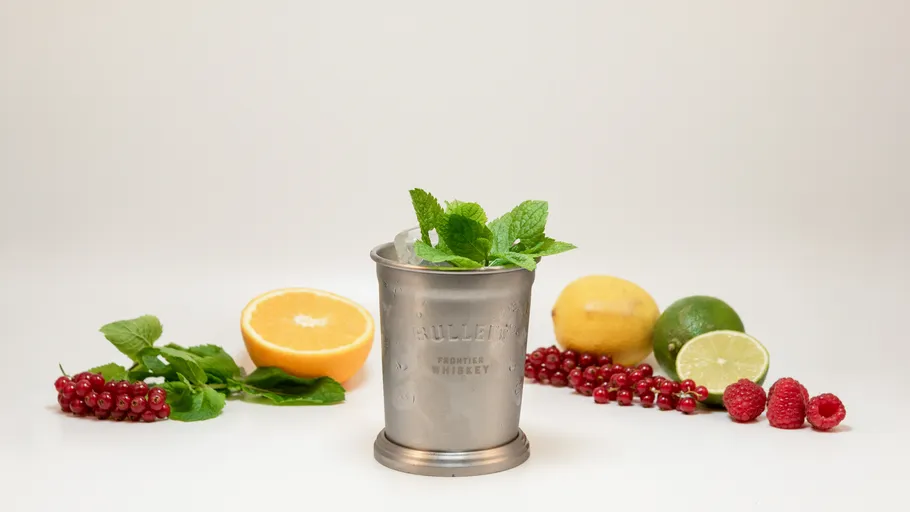 Metal cup with mint, surrounded by fruits.