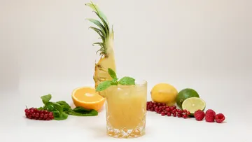 Cocktail mit Ananasgarnitur, umgeben von Früchten.