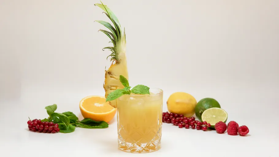 Cocktail with pineapple garnish, surrounded by fruits.